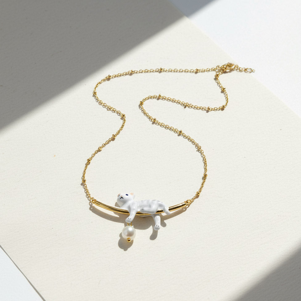 Gold necklace with a white cat pendant on a light surface