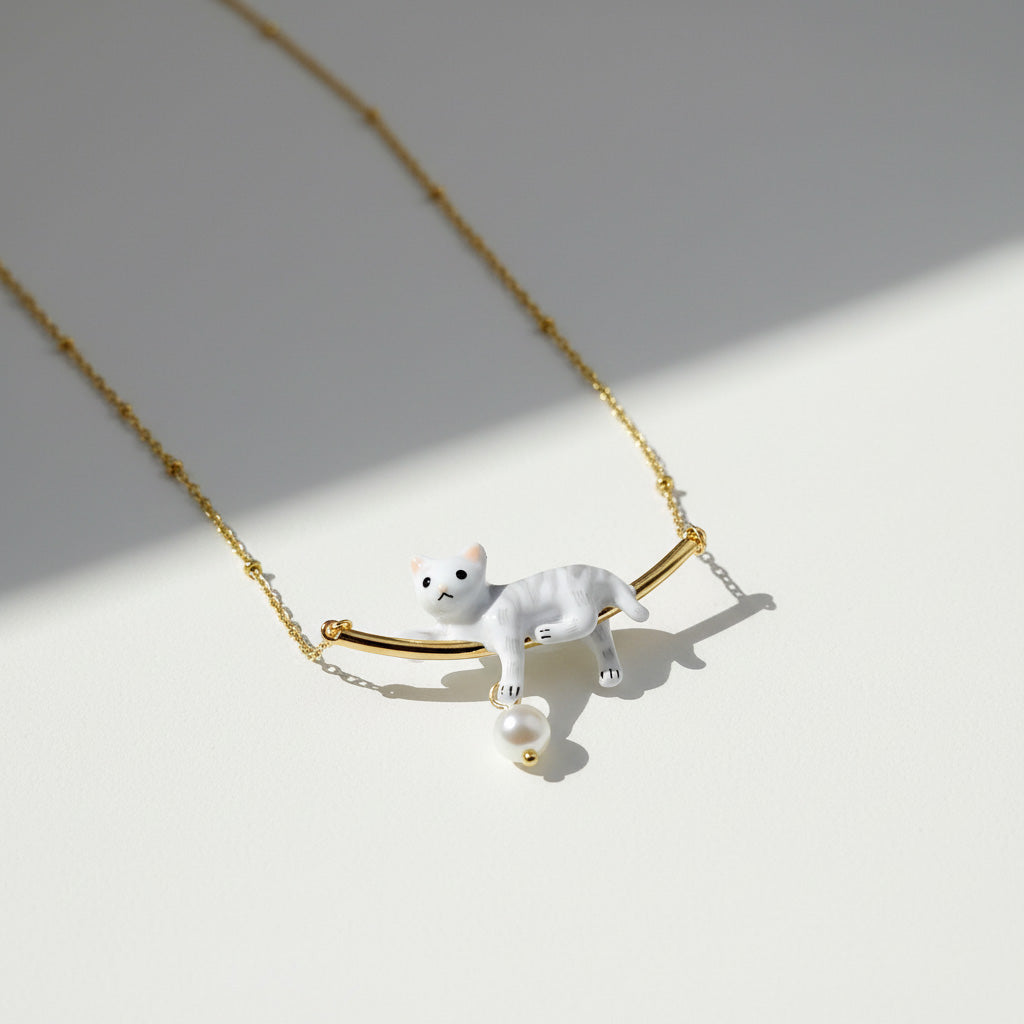 Necklace with a white cat pendant on a gold chain against a light background