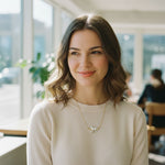 Woman wearing a beige sweater with a gold necklace in a bright indoor setting