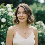 Woman with short brown hair wearing a white top and necklace in a garden setting