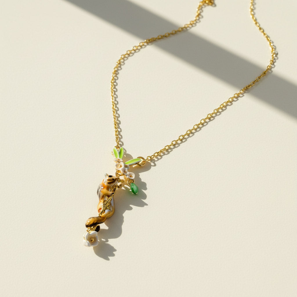 Gold necklace with hand-painted chipmunk and floral vine pendant featuring green leaves and white enamel flowers.