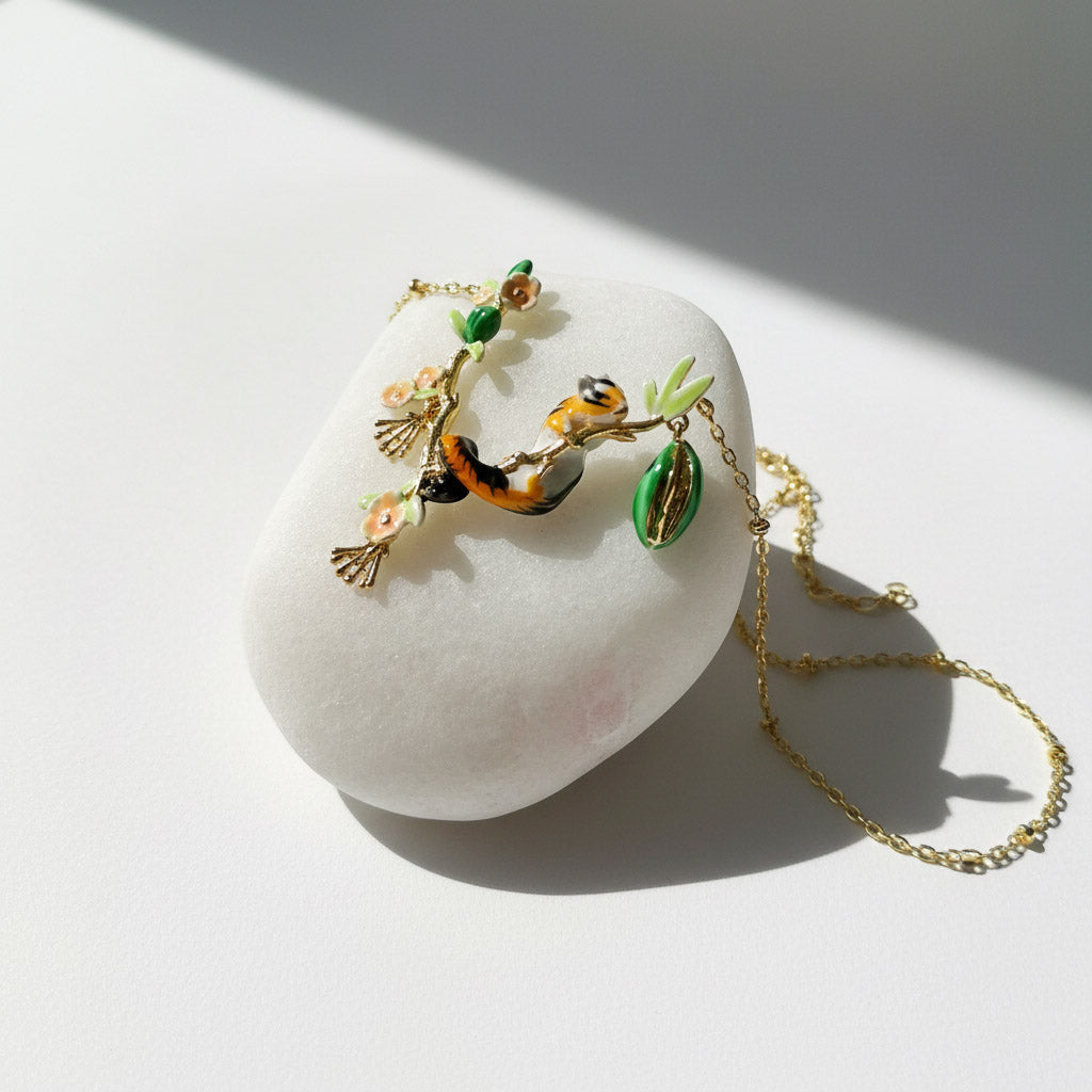 Delicate gold necklace with nature-themed pendant on a white stone surface