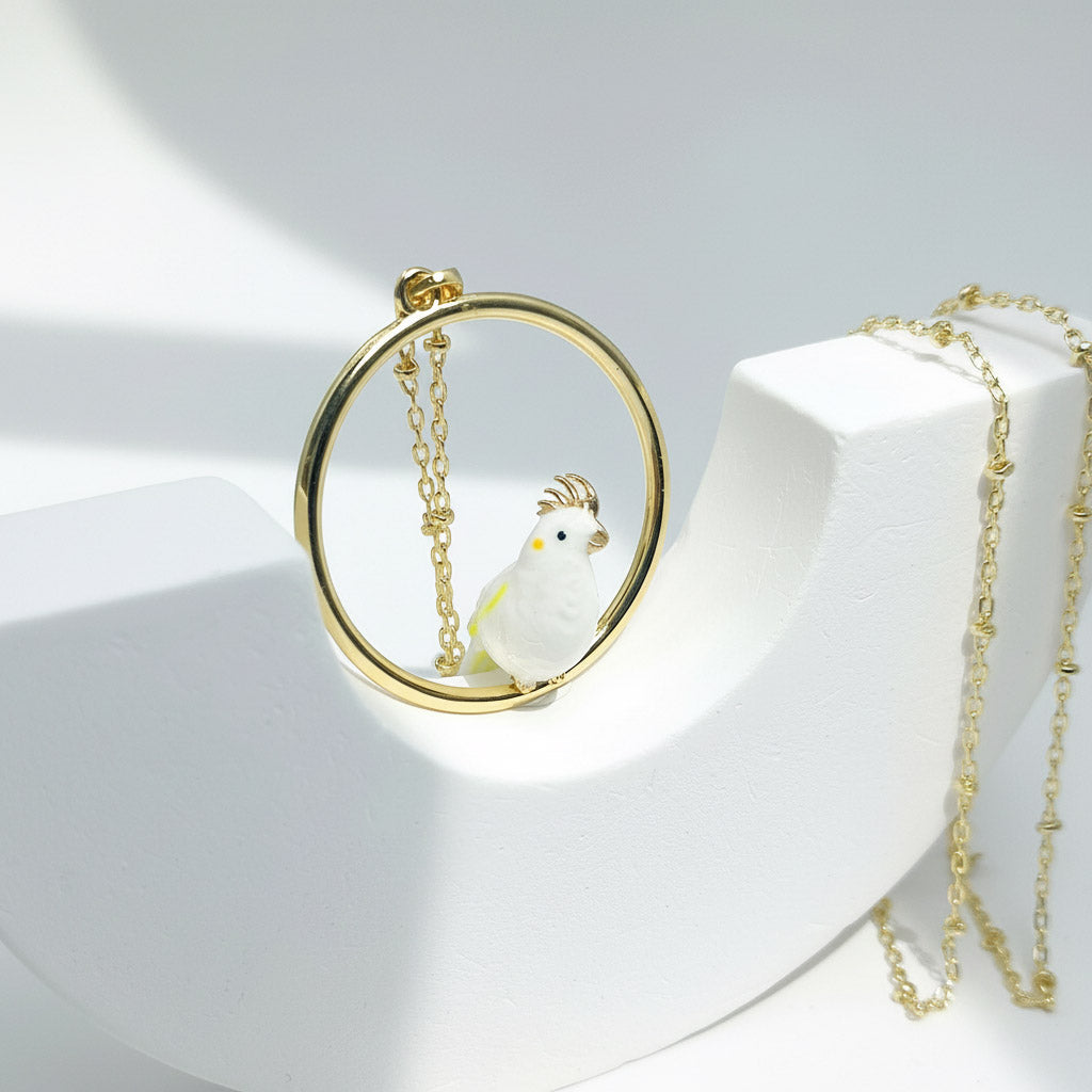 Gold necklace with a round pendant featuring a white cockatoo design on a white background