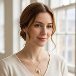 Woman wearing a gold necklace with a pendant in a softly lit room.