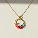 Gold necklace with a circular pendant featuring flowers and a bird on a beige background