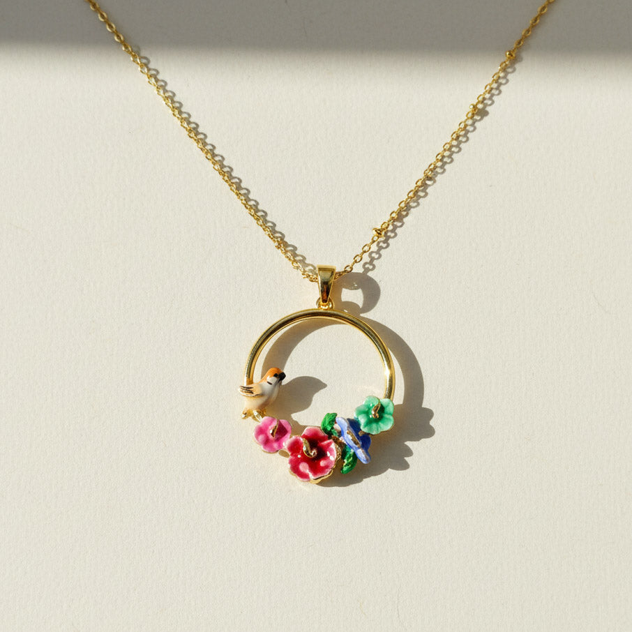 Gold necklace with a circular pendant featuring flowers and a bird on a beige background
