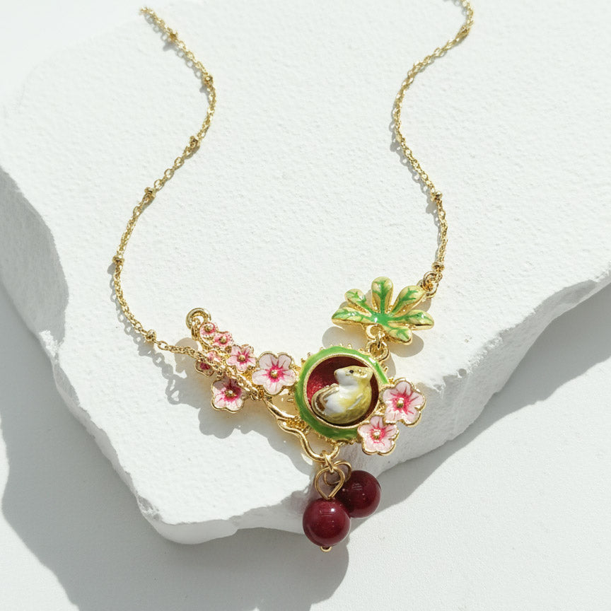 Delicate gold necklace with floral and bird-themed pendants on a white stone surface