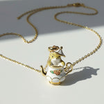 Gold necklace with a teapot-shaped pendant on a light background