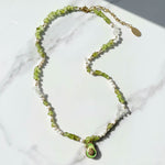Necklace with green beads and a pendant on a marble surface