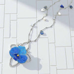Necklace with a blue flower pendant on a white tiled background