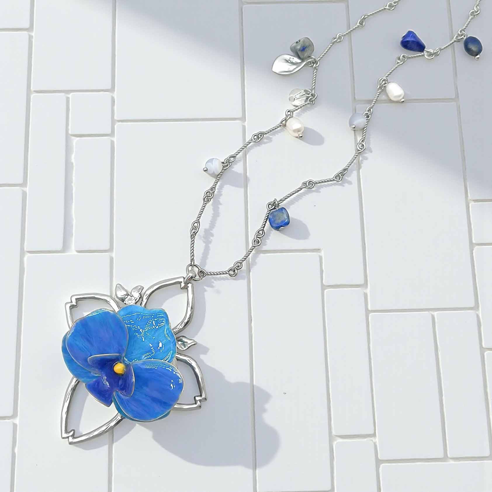 Necklace with a blue flower pendant on a white tiled background