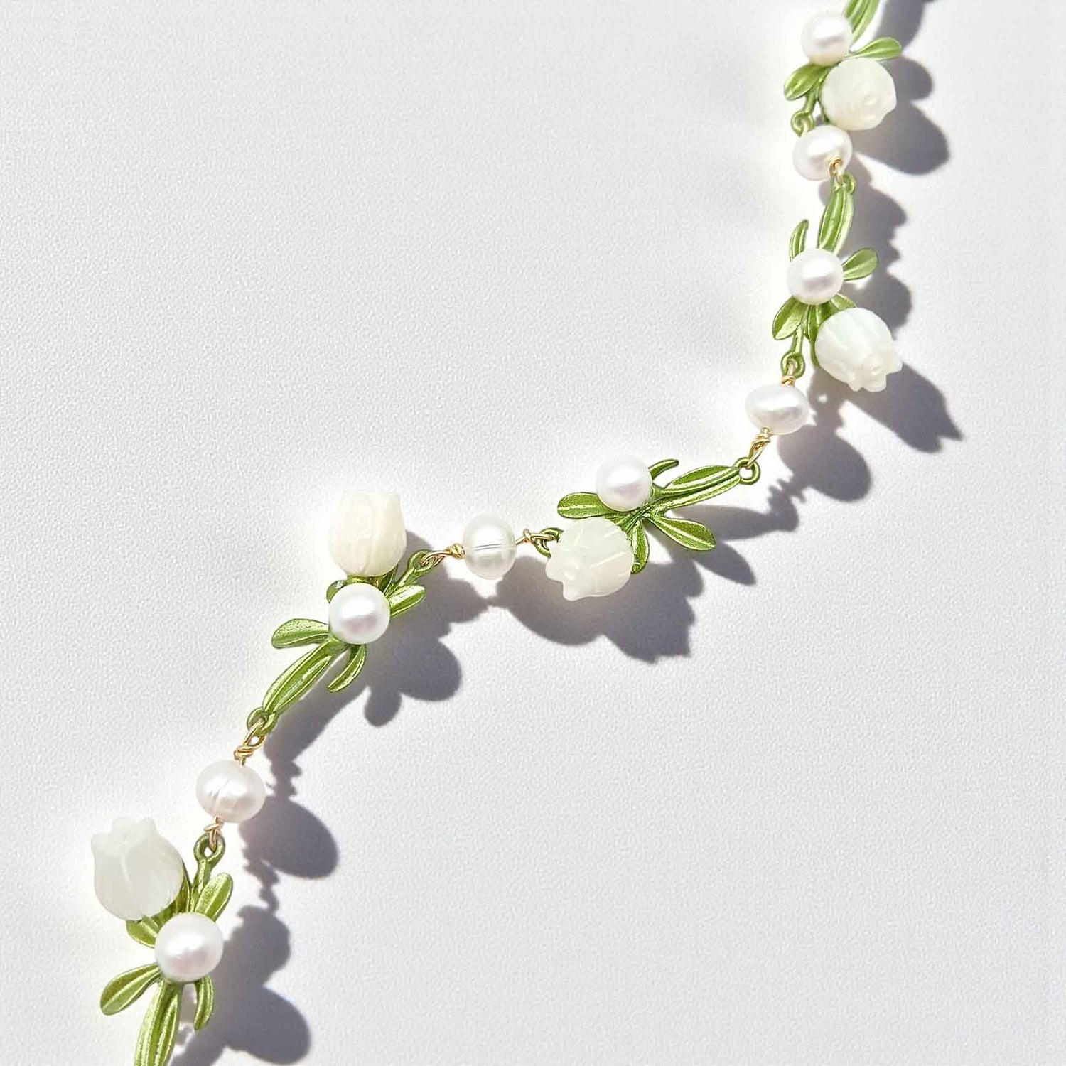 Necklace with white flowers and green leaves on a light gray background