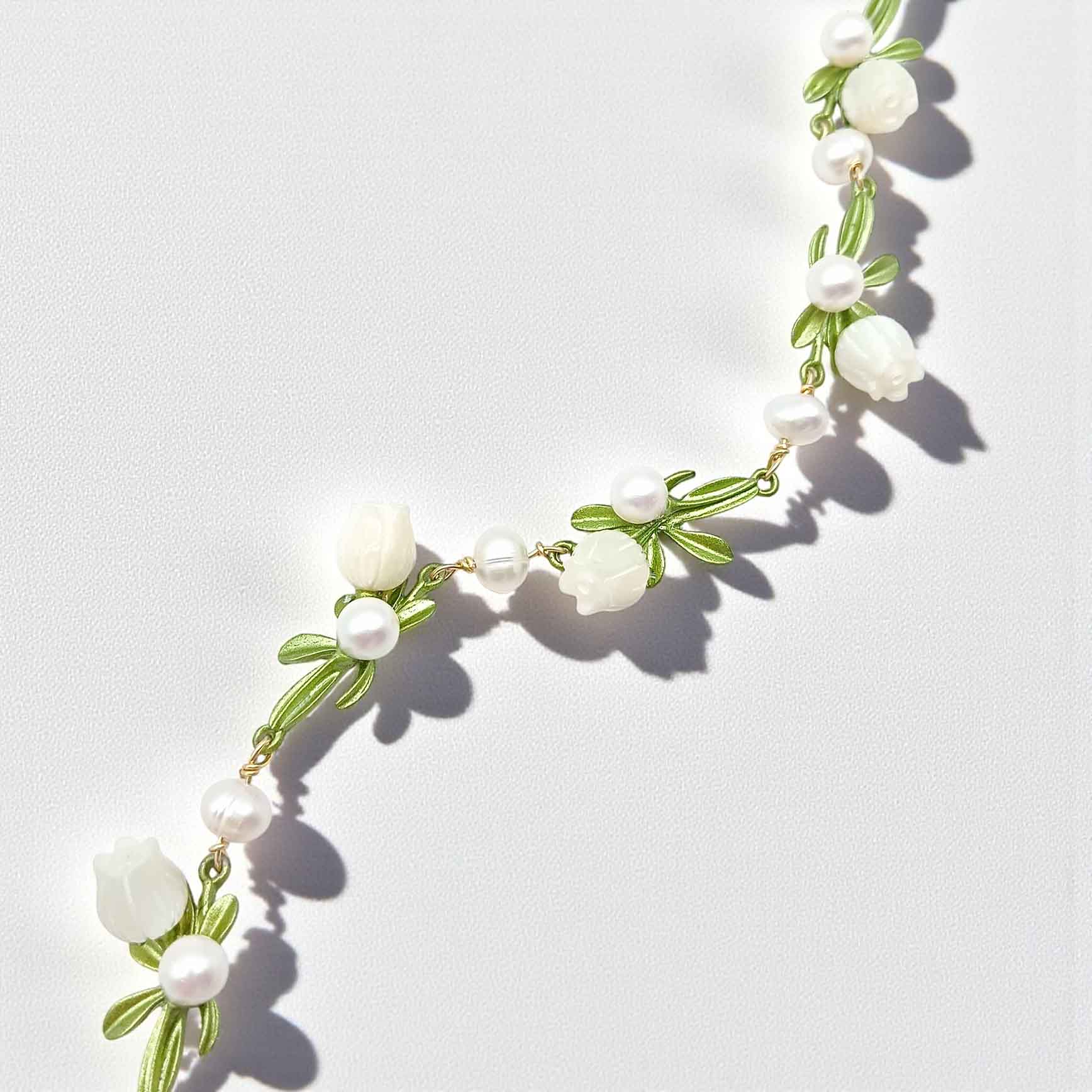 Necklace with white flowers and green leaves on a light gray background