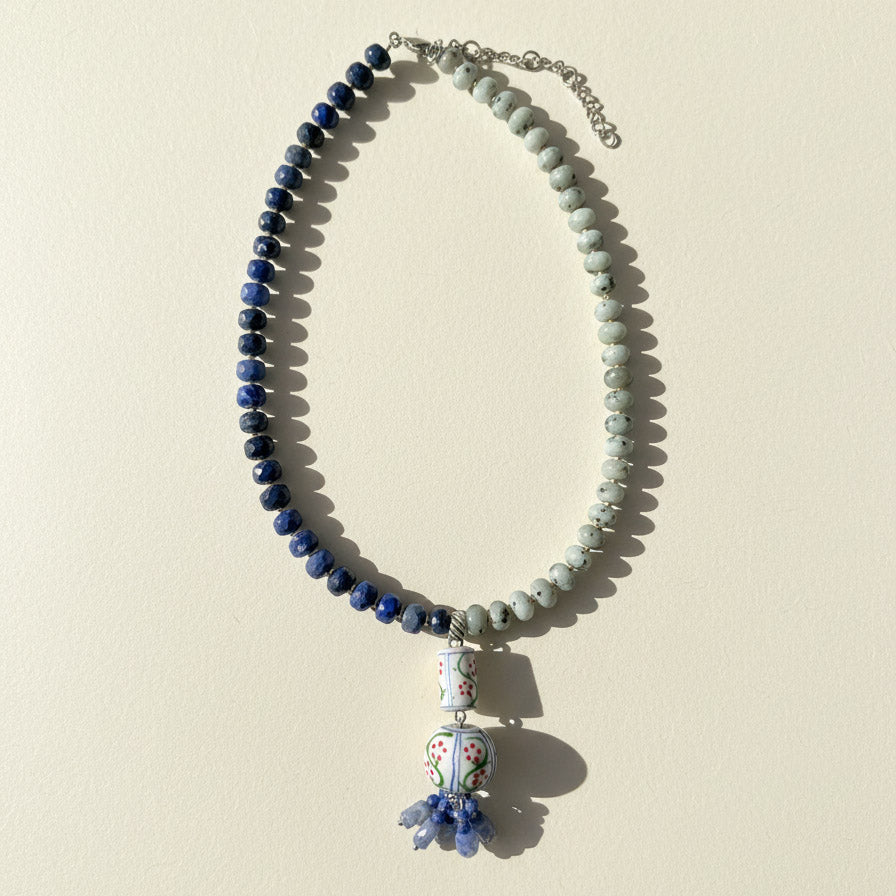 Necklace with blue and green beads and a decorative pendant on a beige background