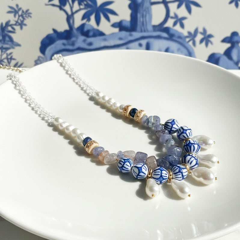 Handcrafted necklace with blue ceramic beads, freshwater pearls, and tanzanite stones on white plate.