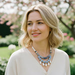 Woman wearing blue and pearl beaded necklace with gold accents in a garden setting.
