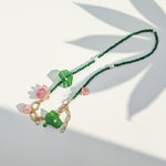 Green and pink floral necklace with gold chain under sunlight.