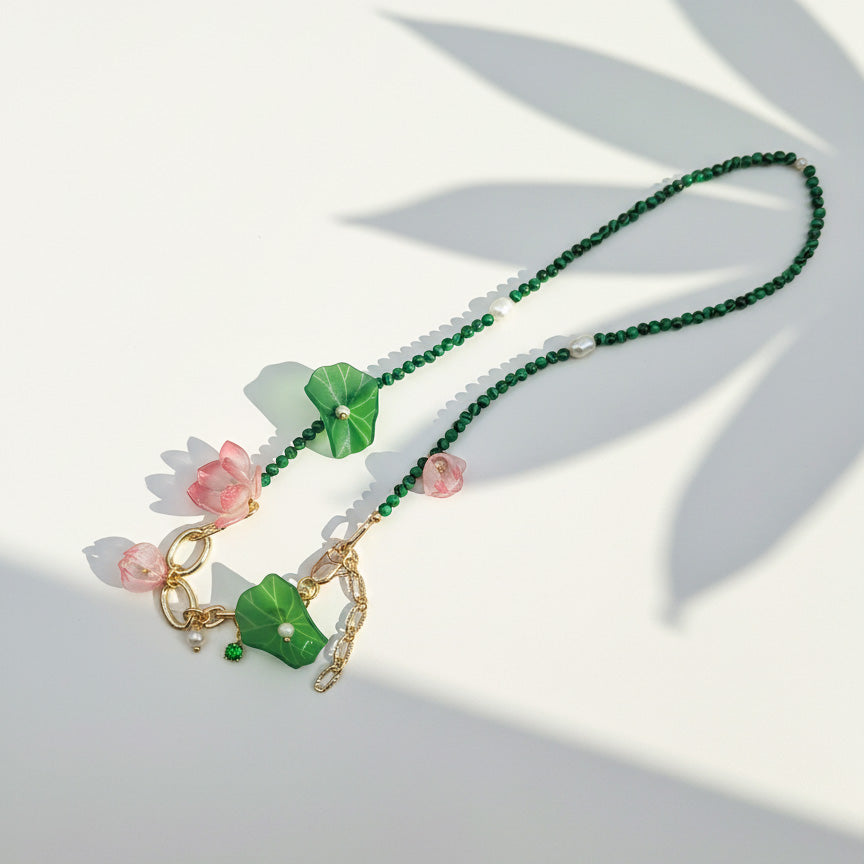Green and pink floral necklace with gold chain under sunlight.