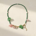 Green malachite and pink blossom beaded necklace with pearls on white background.