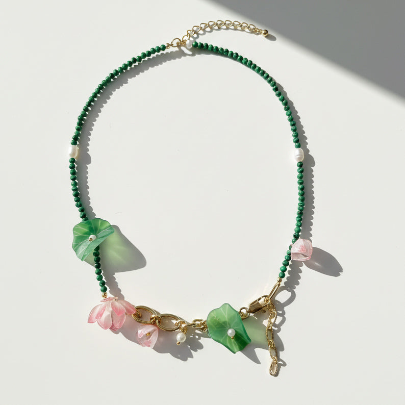 Green malachite and pink blossom beaded necklace with pearls on white background.