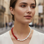 Woman wearing a red coral and pearl necklace against a blurred street background