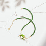 Green beaded necklace with enamel leaf and pearl pendant on cracked white background with sunlight and leaf shadows