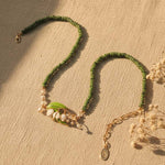 Green beaded necklace with gold chain on a beige surface