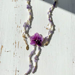Necklace with purple orchid flower and beads on a white surface
