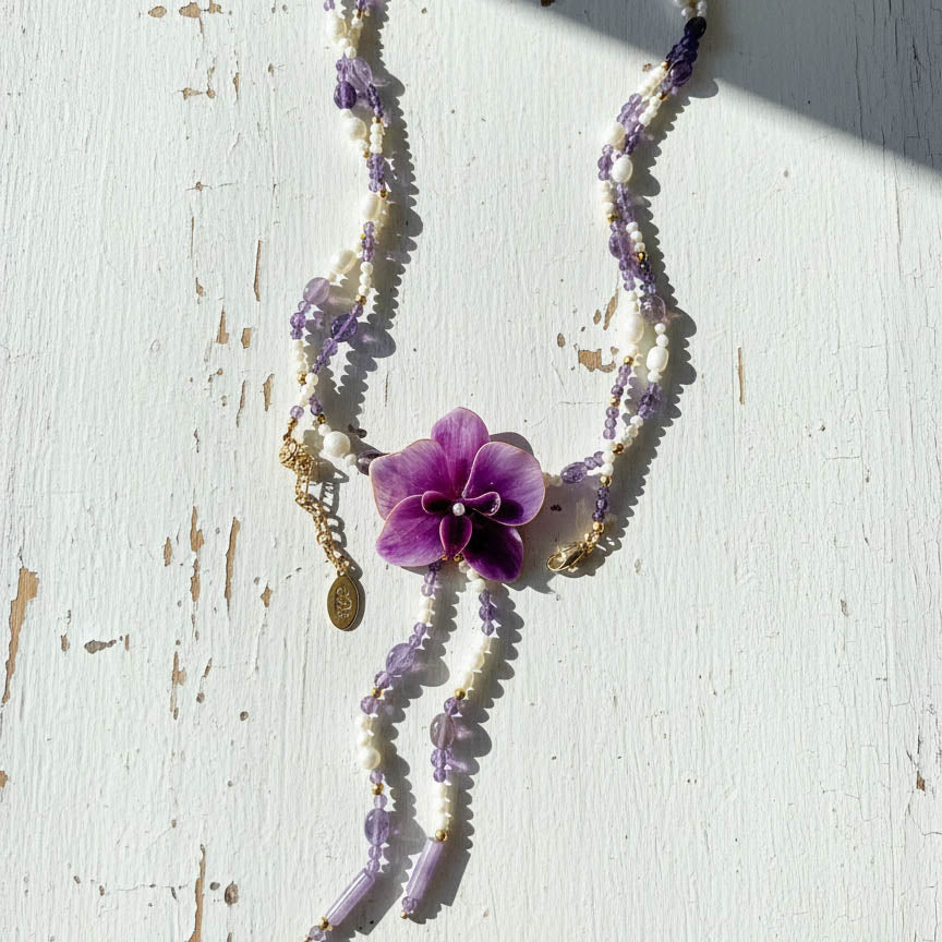 Necklace with purple orchid flower and beads on a white surface