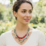 Model wearing coral and turquoise gemstone necklace outdoors.