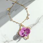 Gold necklace with a purple flower pendant on a marble surface