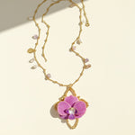 Gold necklace with a pink orchid pendant on a beige background