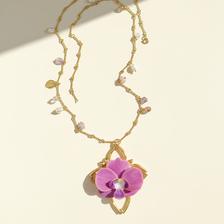 Gold necklace with a pink orchid pendant on a beige background