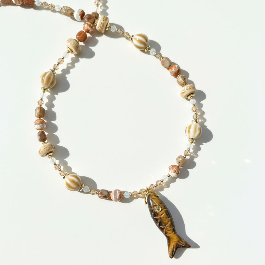 Handmade beaded necklace with brown ceramic beads and carved fish pendant on white background