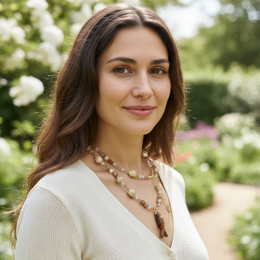 Model wearing long beaded necklace with natural stones and carved fish pendant outdoors
