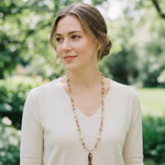 Model wearing extra long earthy toned gemstone necklace with carved fish pendant