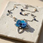 Necklace with a blue forchid pendant on a textured surface