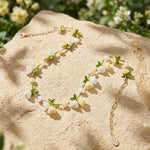 Spring Blossom Garden Necklace with Glass Flowers, Semi-Precious Stones and Enamel Leaves on a textured surface with greenery in the background