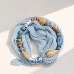 Artisan pleated scarf necklace with navy printed scarf, porcelain beads, woven rattan beads and pearl magnetic clasp on a neutral background.