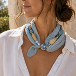 Woman wearing an artisan pleated scarf necklace with navy printed scarf, porcelain beads, woven rattan beads and a pearl magnetic clasp.
