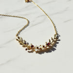 Gold necklace with leaf design and embedded stones on a light background