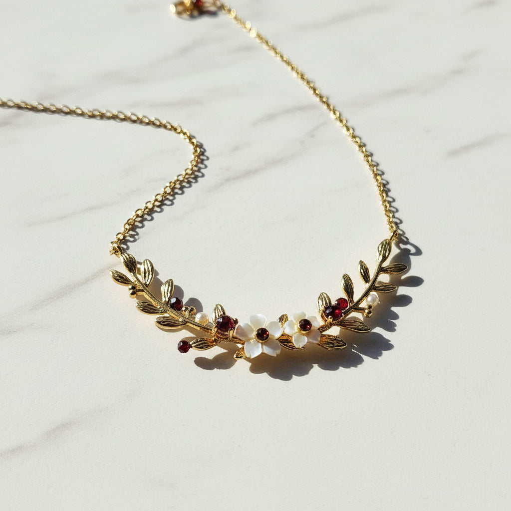 Gold necklace with leaf design and embedded stones on a light background