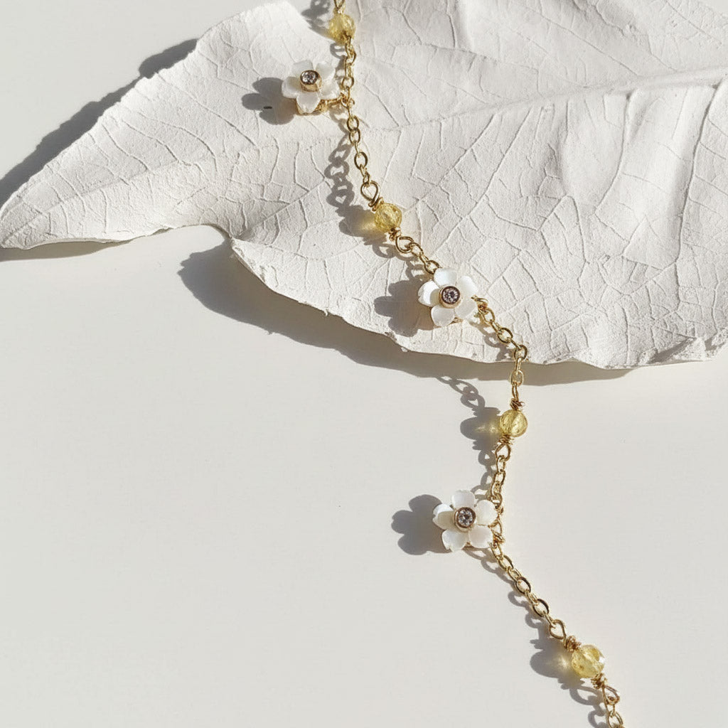 Delicate gold necklace with floral pendants on a white leaf background