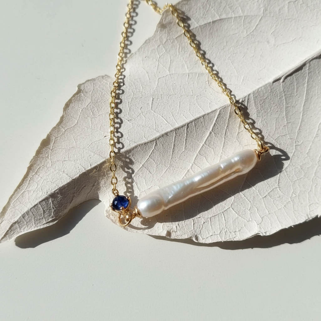 Necklace with a bar-shaped pearl pendant and blue gemstone on a leaf background