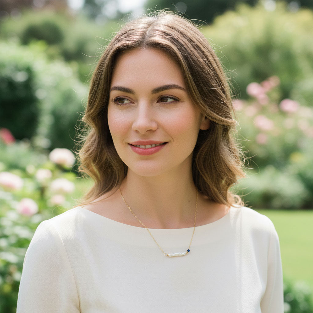 Woman with shoulder-length brown hair standing in a garden with blurred greenery and flowers in the background