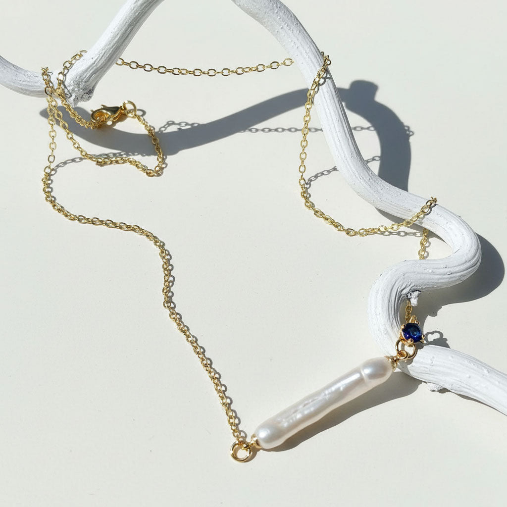 Gold necklace with pearls and a blue gemstone on a white surface