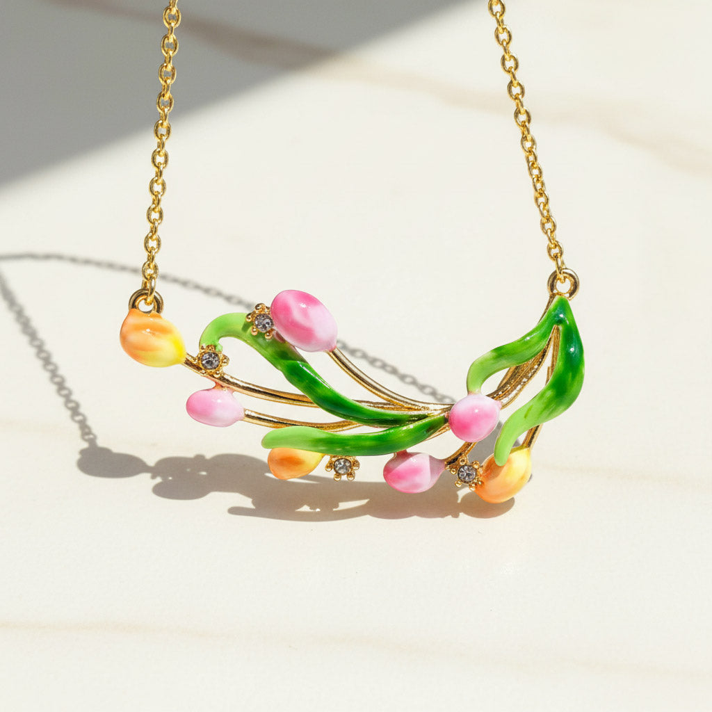 Close-up of a gold chain necklace featuring a hand-painted tulip pendant with pink, orange, and green enamel flowers and small crystal accents.