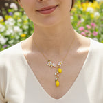 Woman wearing a delicate necklace with floral and lemon pendants against a blurred floral background