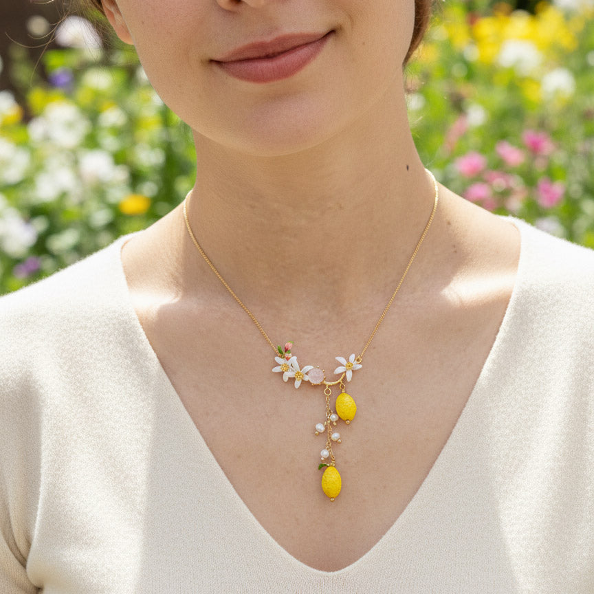 Woman wearing a delicate necklace with floral and lemon pendants against a blurred floral background
