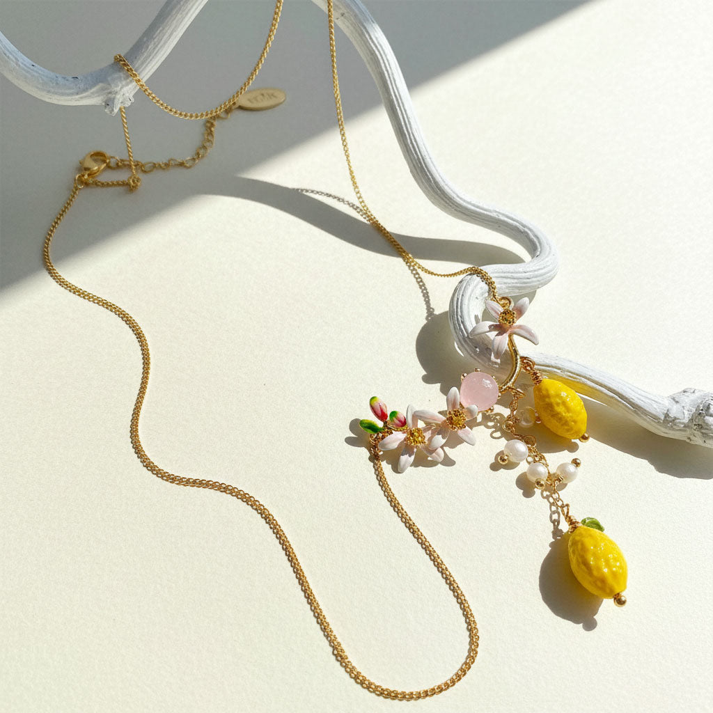 Gold necklace with floral and fruit pendants on a white surface